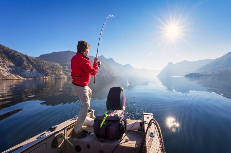 Sport fisherman on a boat with his rod bent after a catch in an alpine lake.
