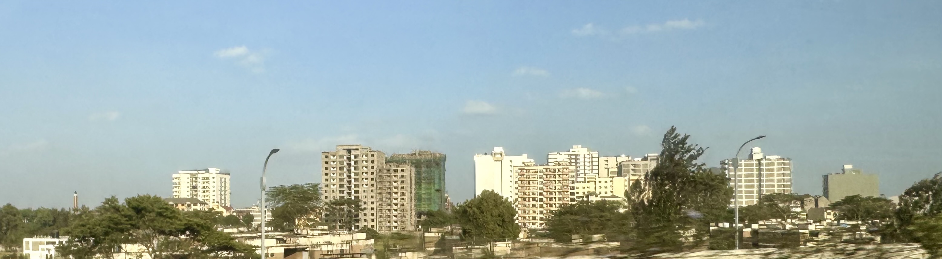 Wide city skyline with mid‑rise apartment buildings and trees in the foreground, seen under a clear blue sky.