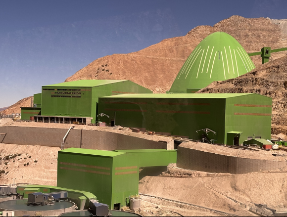 Large green industrial processing facility set into a rocky desert landscape with surrounding hills.