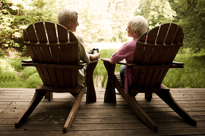 Rear view of a senior couple relaxing in Adirondack chairs on a wooden deck. Horizontal shot.