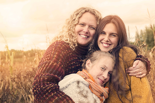 Portrait of teenagers with mother in autumn sunset outdoors. They are snuggling together, standing in a corn field. They all are wearing warm wool pullover. Waist up horizontal shot with sun flare and copy space. This was taken in Quebec, Canada.